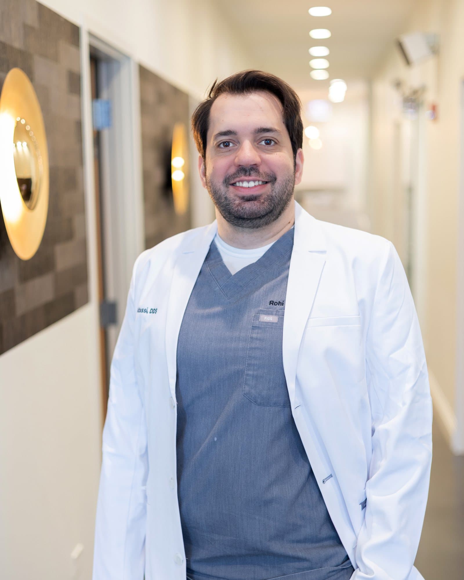 Dr. Atassi in a white coat, smiling, in the practice hallway