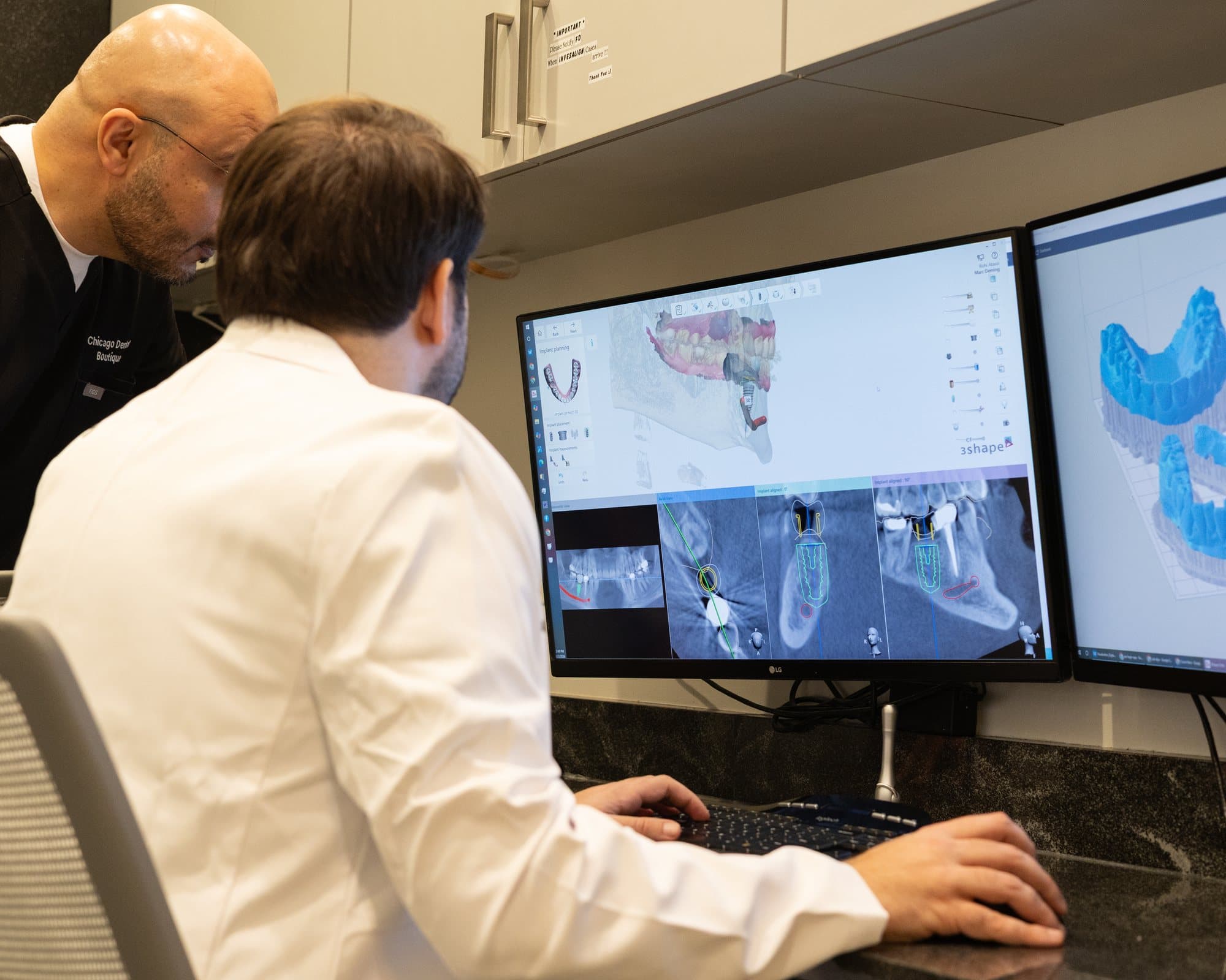 Dr. Atassi reviewing an implant plan on screen with a colleague looking on
